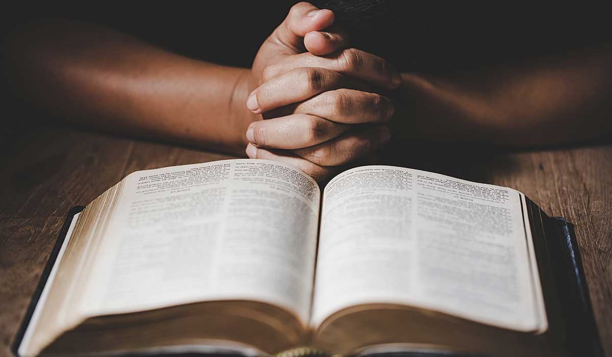 pessoa orando em frente a uma biblía